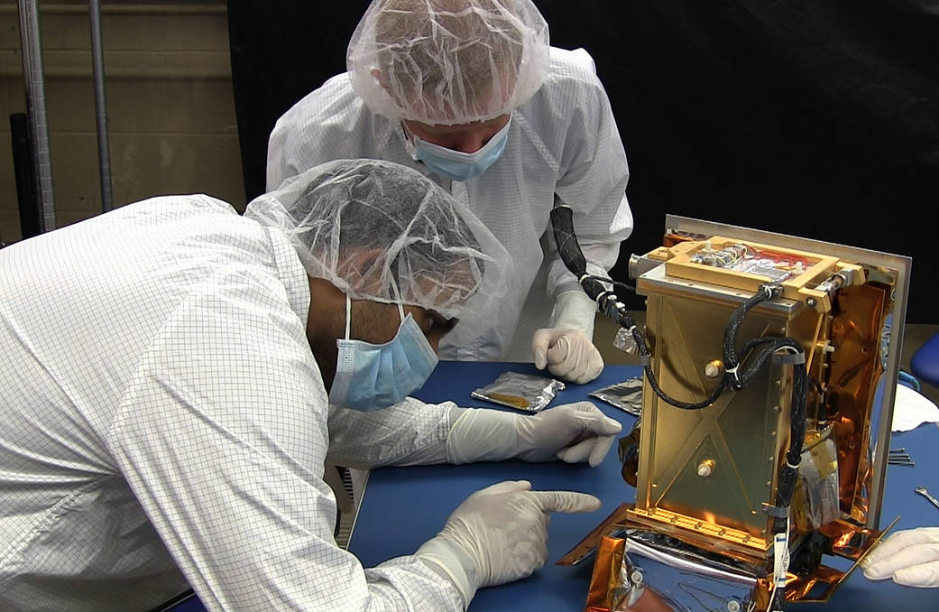 Two people in protective gear examine hardware