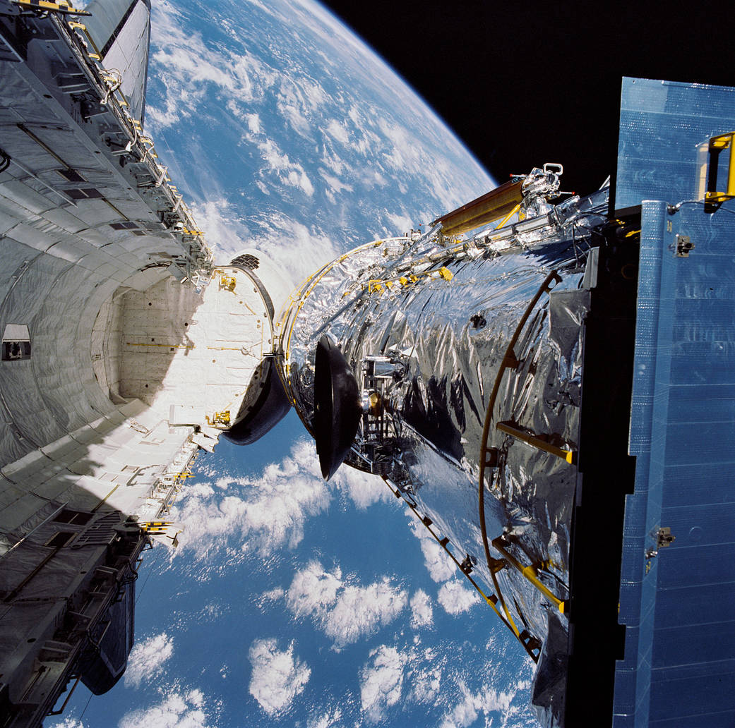 Space shuttle cargo bay open and space telescope being released, with Earth visible below