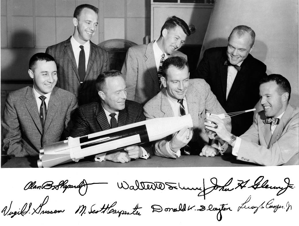 Seven Mercury astronauts around table with model of rocket