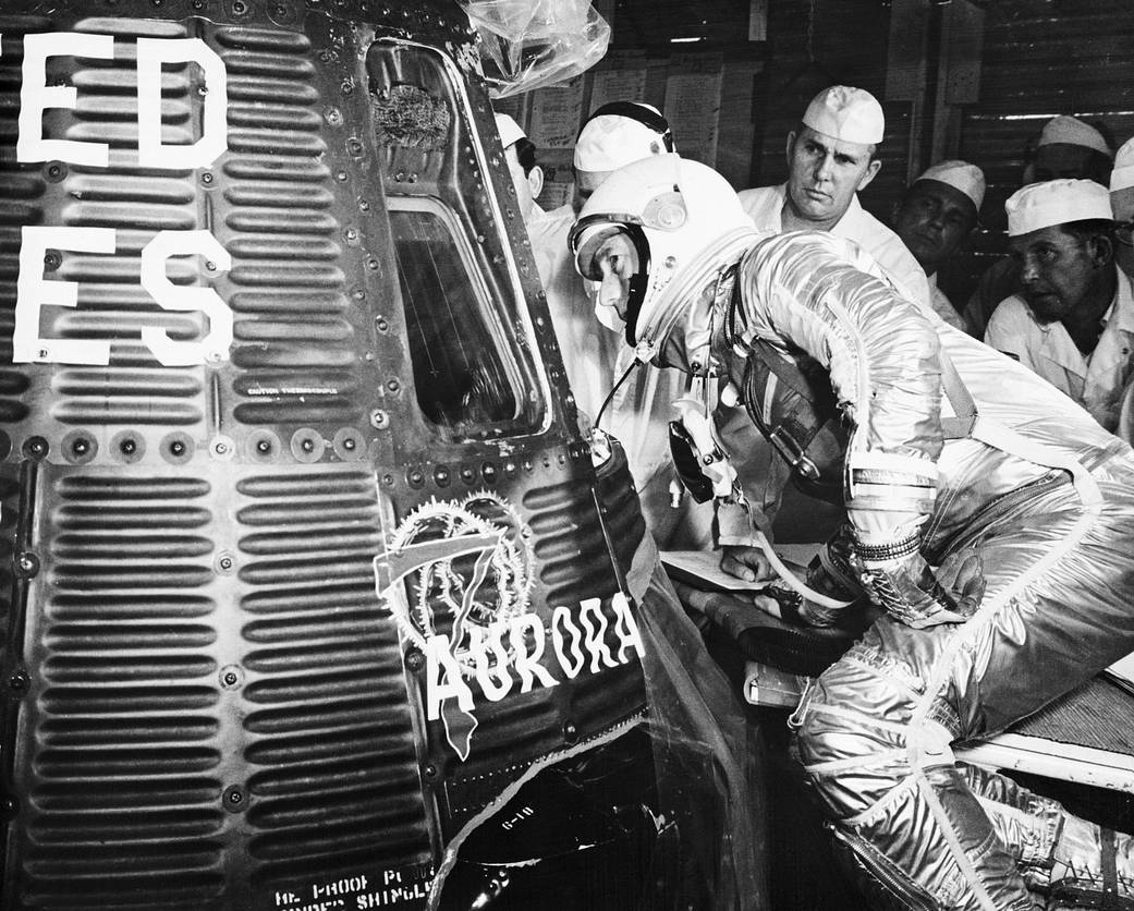 Astronaut in silver spacesuit looking into spacecraft from outside