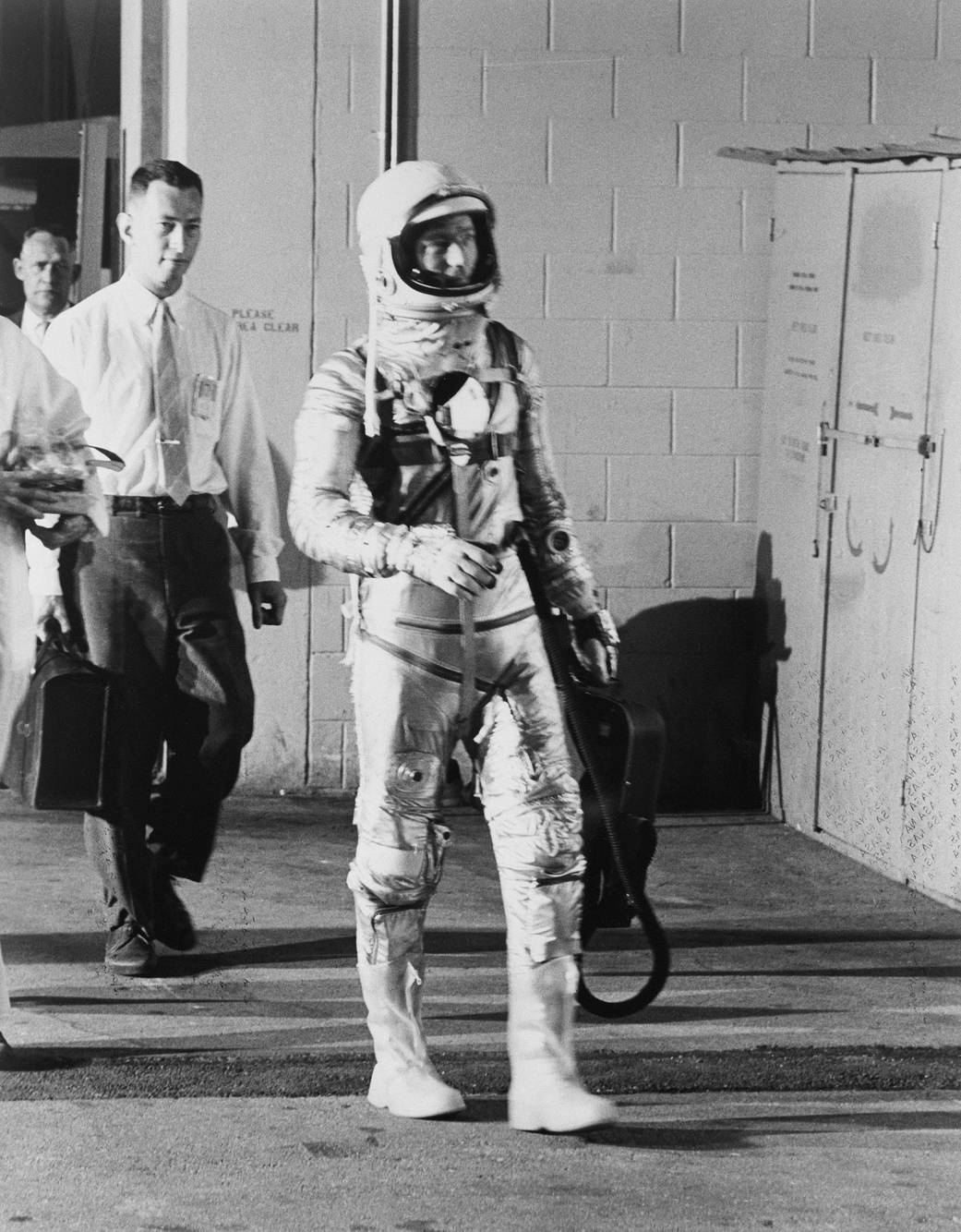 Scott Carpenter in spacesuit walks out of building toward launch site