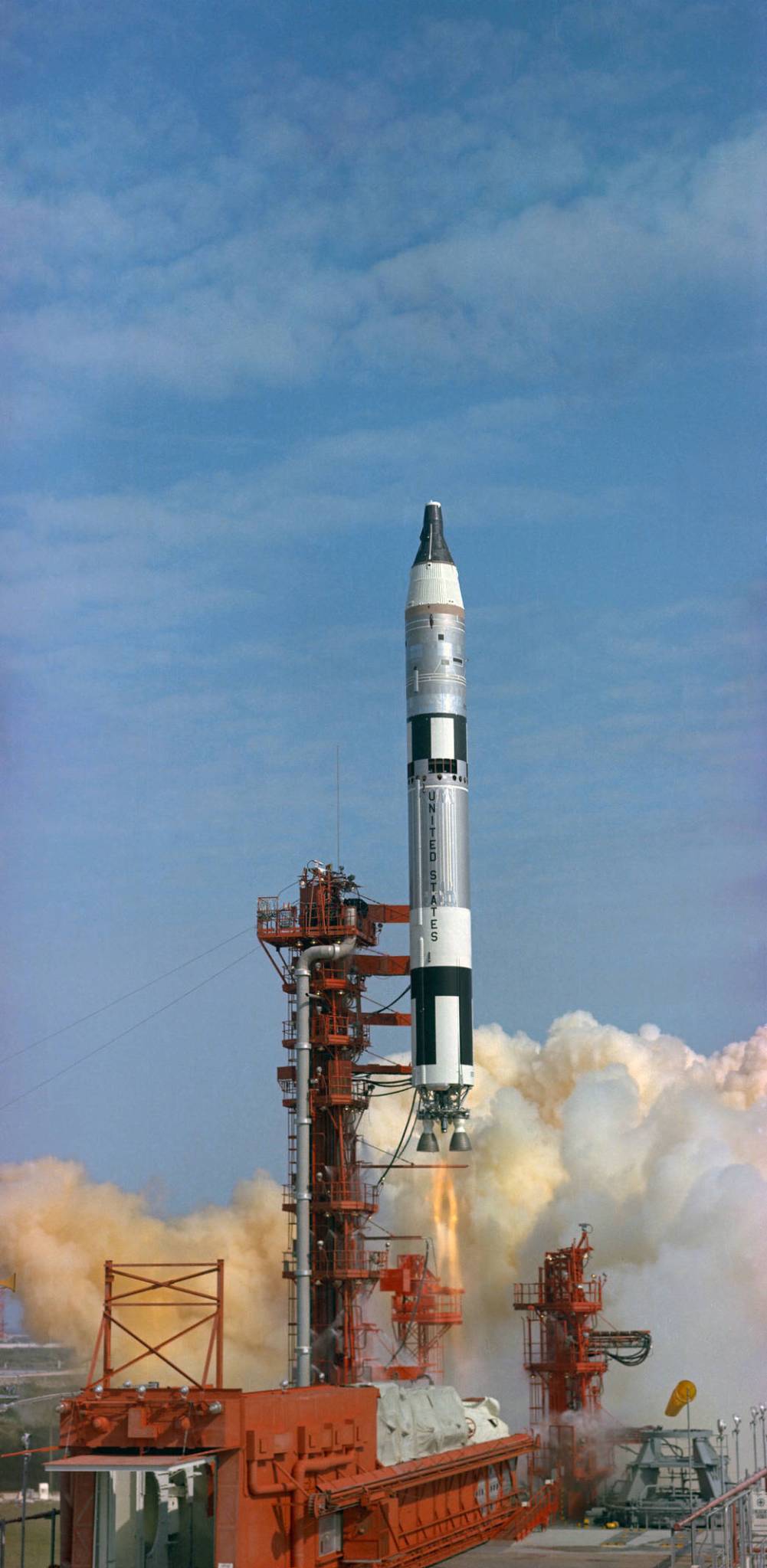 Daytime launch of Gemini-Titan 3, rocket lifting off launch pad with cloud of smoke below
