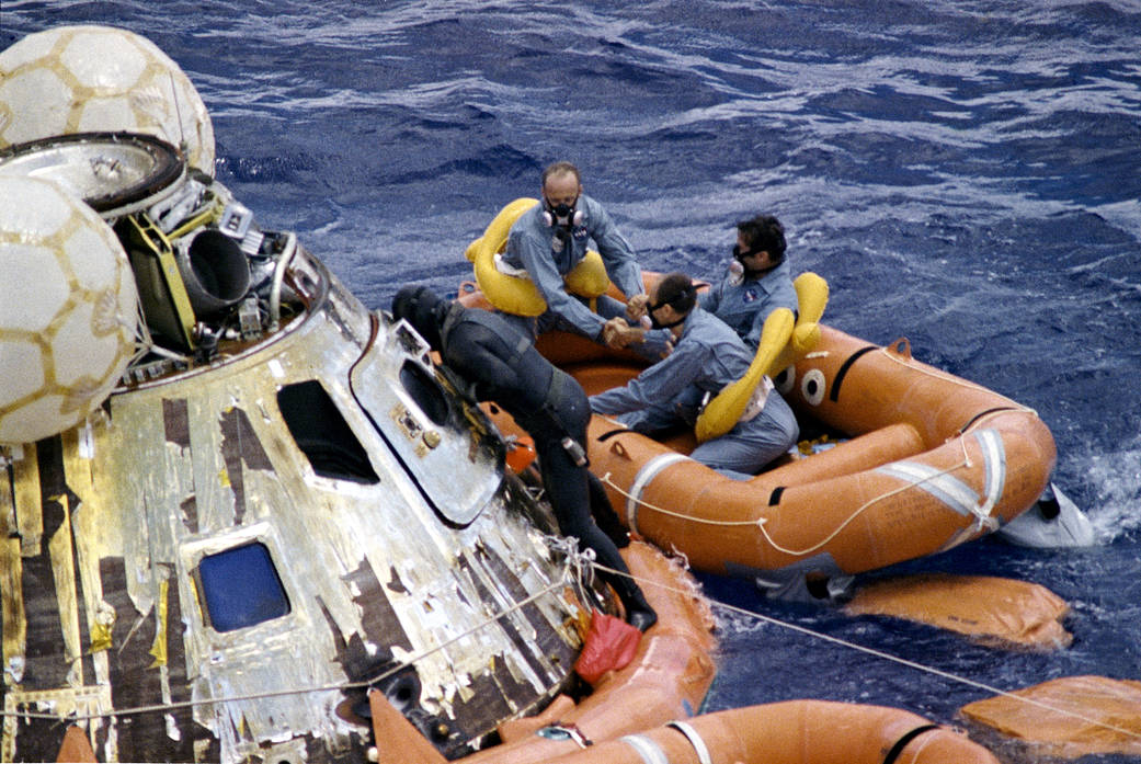 Three astronauts in flight suits recovered from floating spacecraft