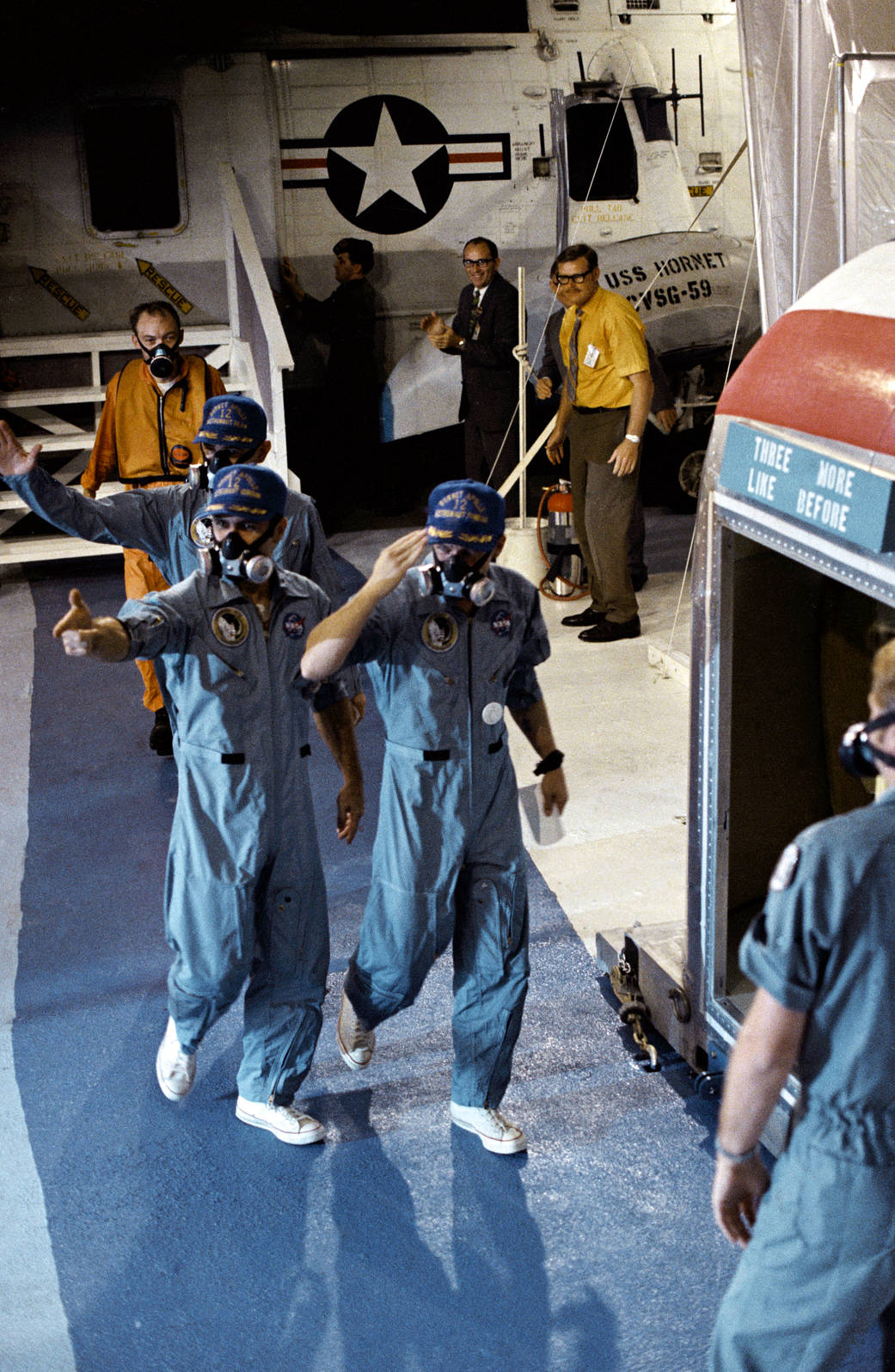 Astronauts in flight suits with protective masks wave