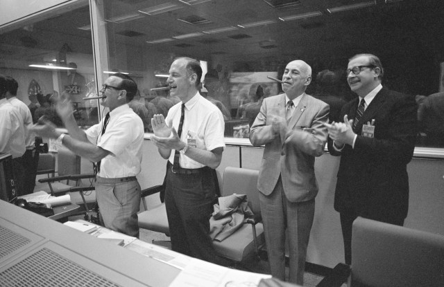 NASA managers applaud the successful splashdown of the Apollo 10 mission from the back row of consoles in the Manned Spacecraft Center's Mission Control Center. Pictured are (from left) MSC Director of Flight Operations Christopher C. Kraft, MSC Deputy Director George Low, MSC Director Robert R. Gilruth, and NASA Administrator Thomas Paine. (26 May 1969)