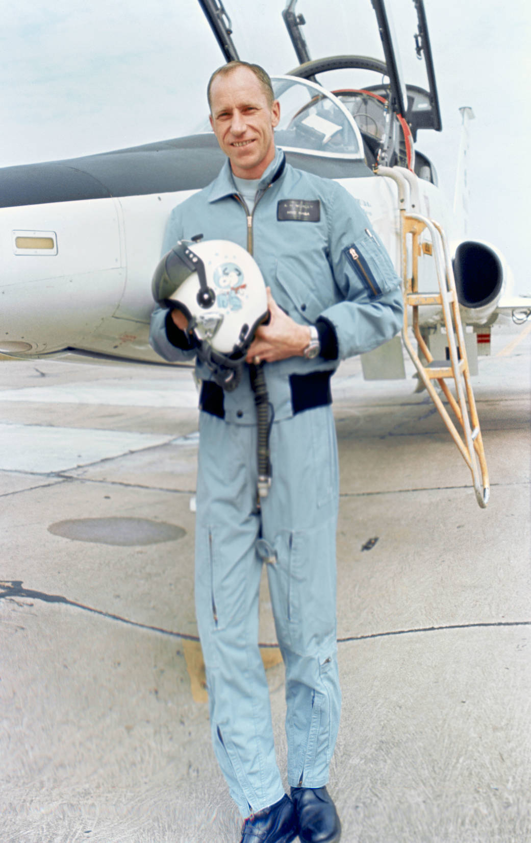 Astronaut Alfred M. Worden standing beside T-38 aircraft and displaying his flying helmet with "Snoopy" cartoon character painte
