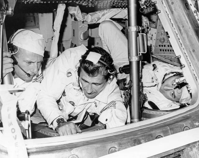 Three astronauts examine spacecraft in facility