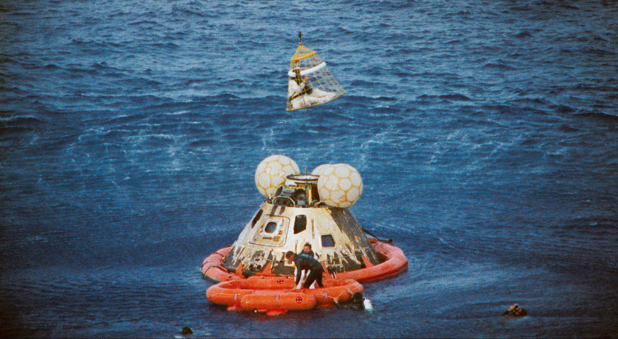 Apollo capsule floating in ocean with recovery team.