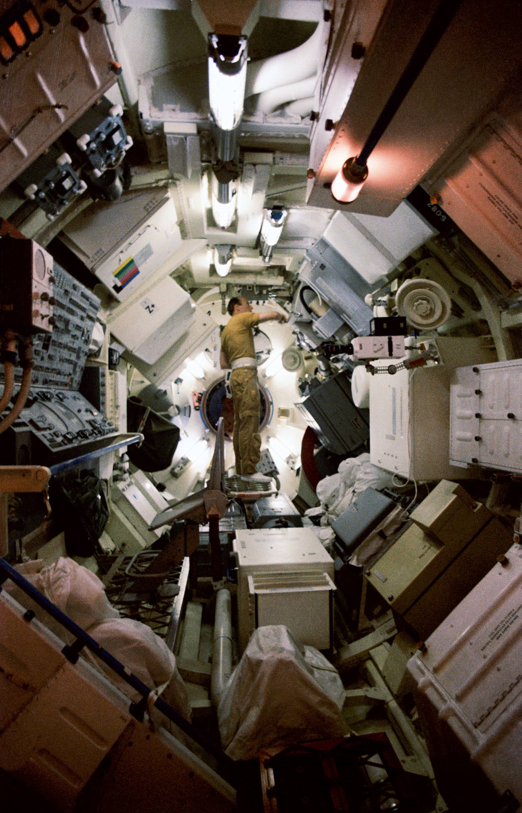 Astronaut in flight suit inside mock space station surrounded by boxes and containers