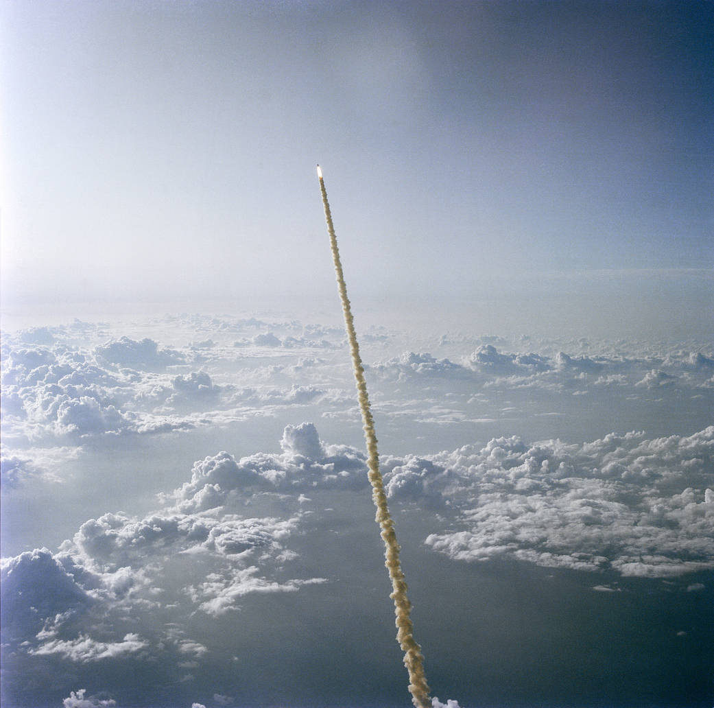 Space shuttle soars upward in sky above a layer of clouds after launch