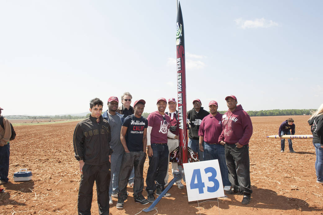 Students stand next to a rocket on the launch pad