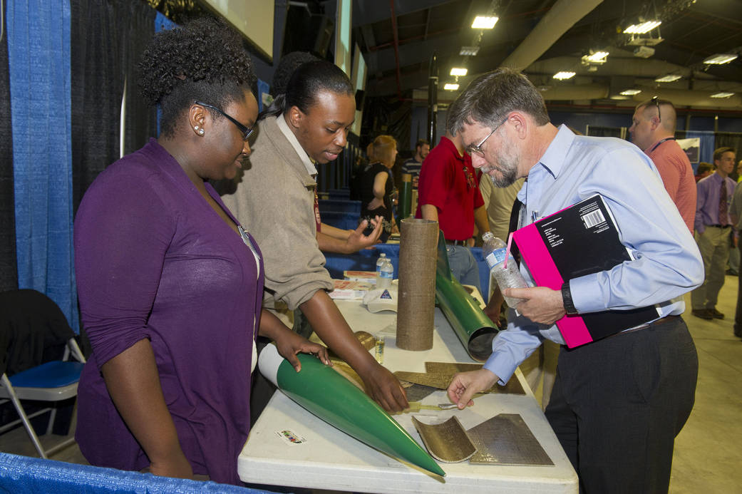 Two students and a NASA employee look at a team's rocket design