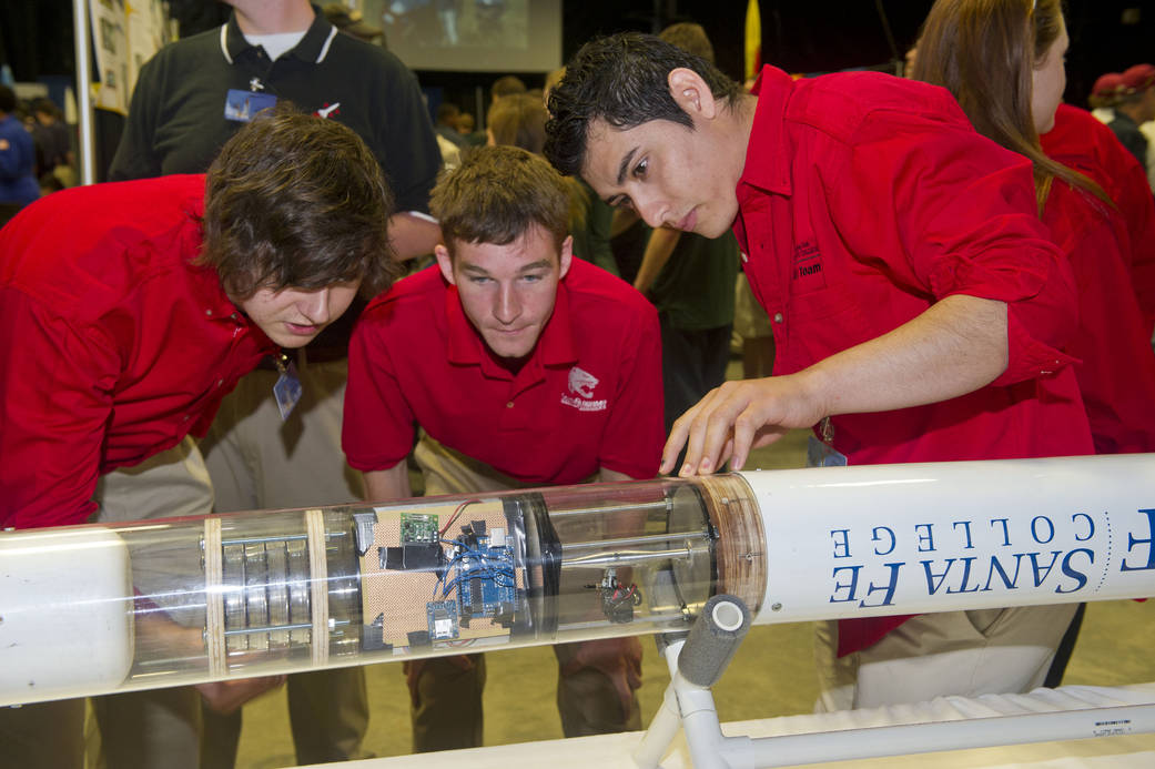 Three students inspect rocket payload