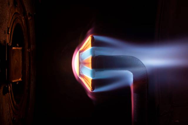 An "umbrella-like" shell held up on a curved stand in a dark testing chamber, heated to the point of looking red with blue wisps blowing past it.