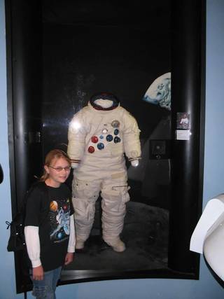 Young woman stands next to a display of a space suit in a museum.