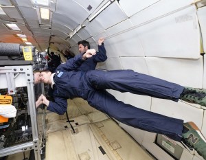 A researcher on a parabolic flight floats horizontally next to his experiment.