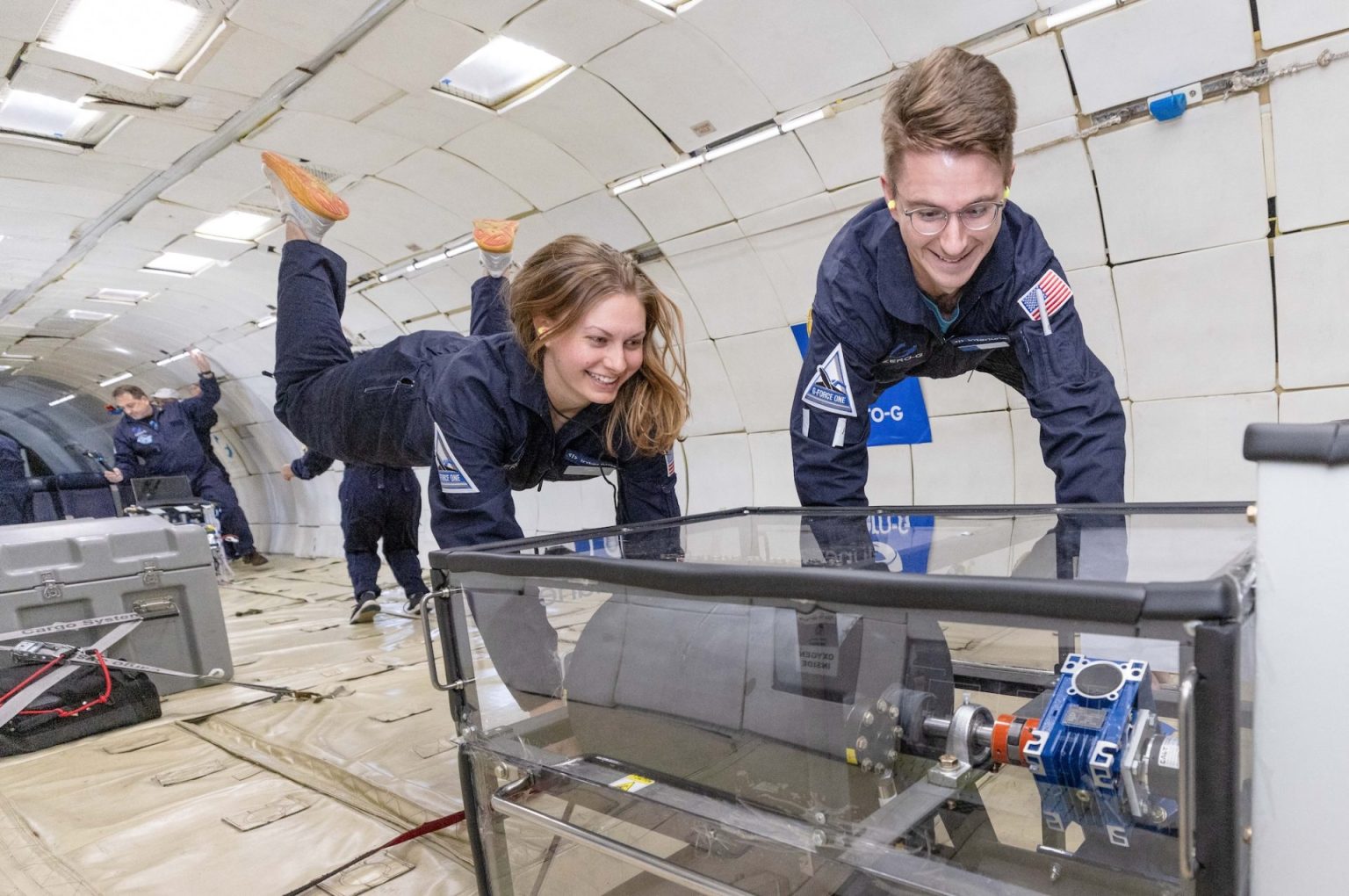 Two researchers float upward while holding onto their experiment on a parabolic flight.
