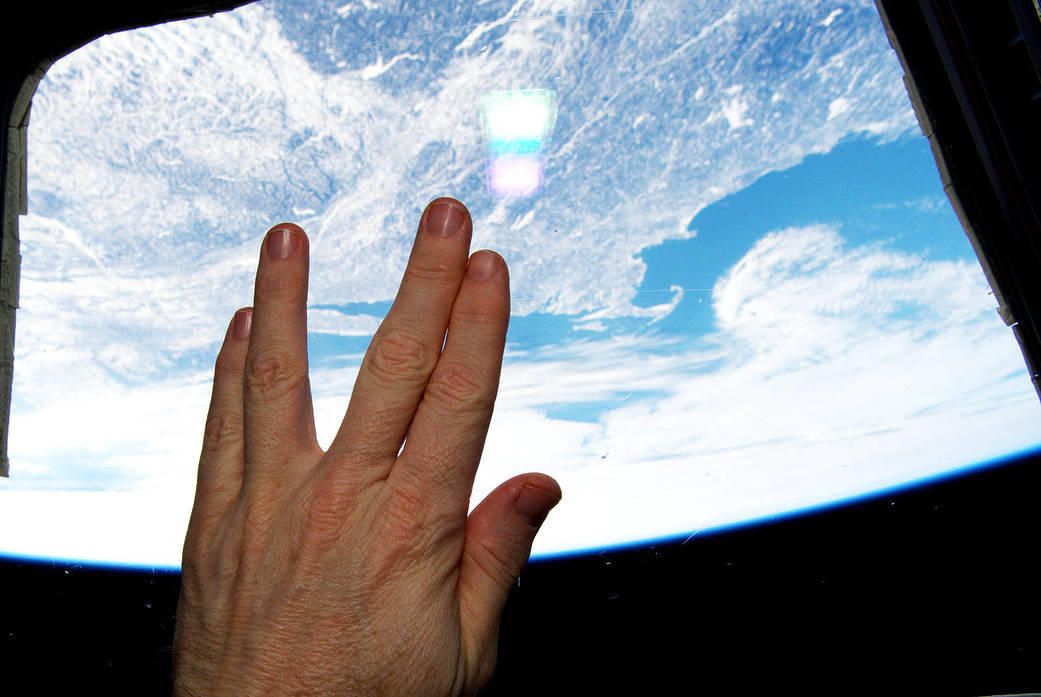 vulcan hand sign in front of window looking out of the international space station