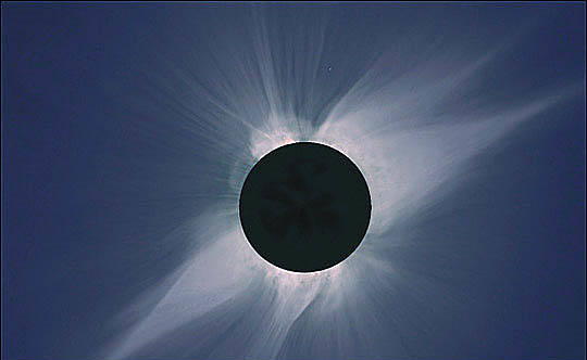 A dark circle with the wispy white corona of the sun projecting out of it