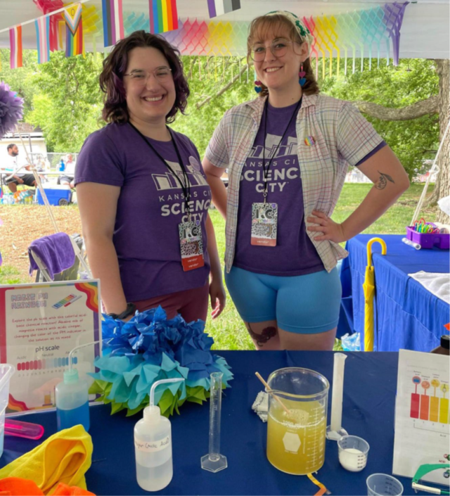 Two smiling people pose in front of a colorful science booth