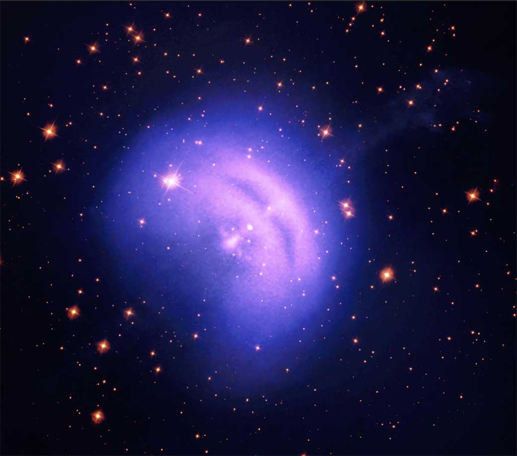 A white spot in the middle of a blue/pink/purple hazy circle. Orange stars are dotted across a black space background.
