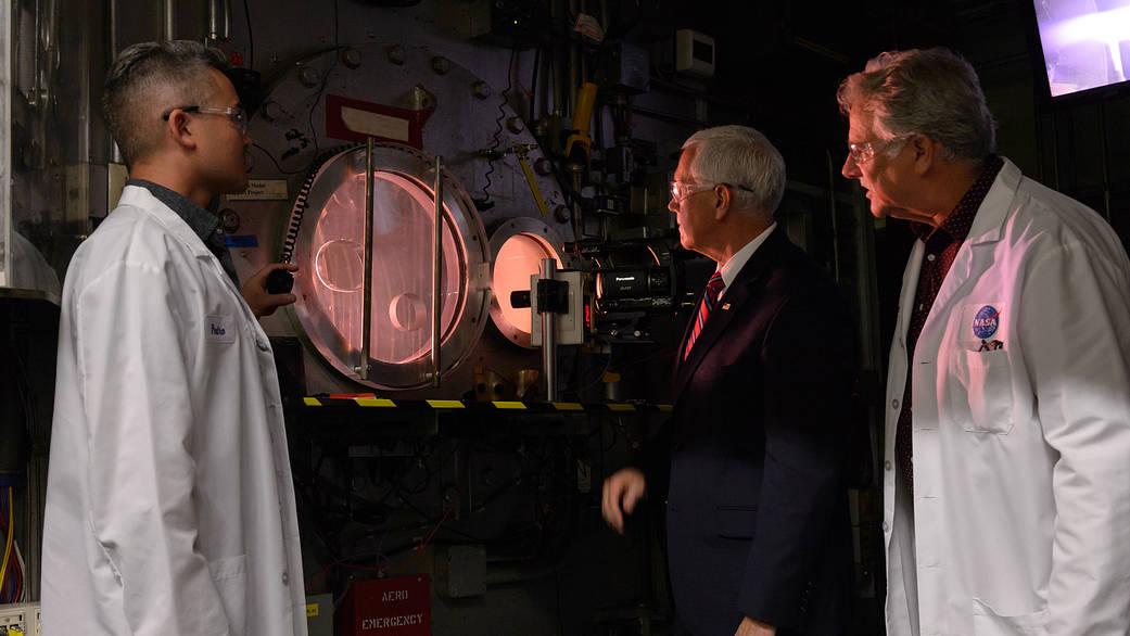 Three people view a test in a high-energy wind tunnel