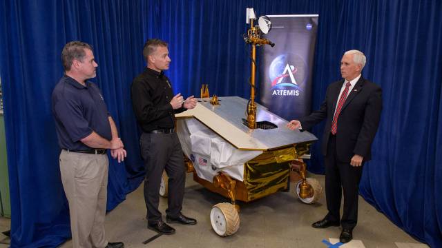 three people stand near a model of a lunar rover