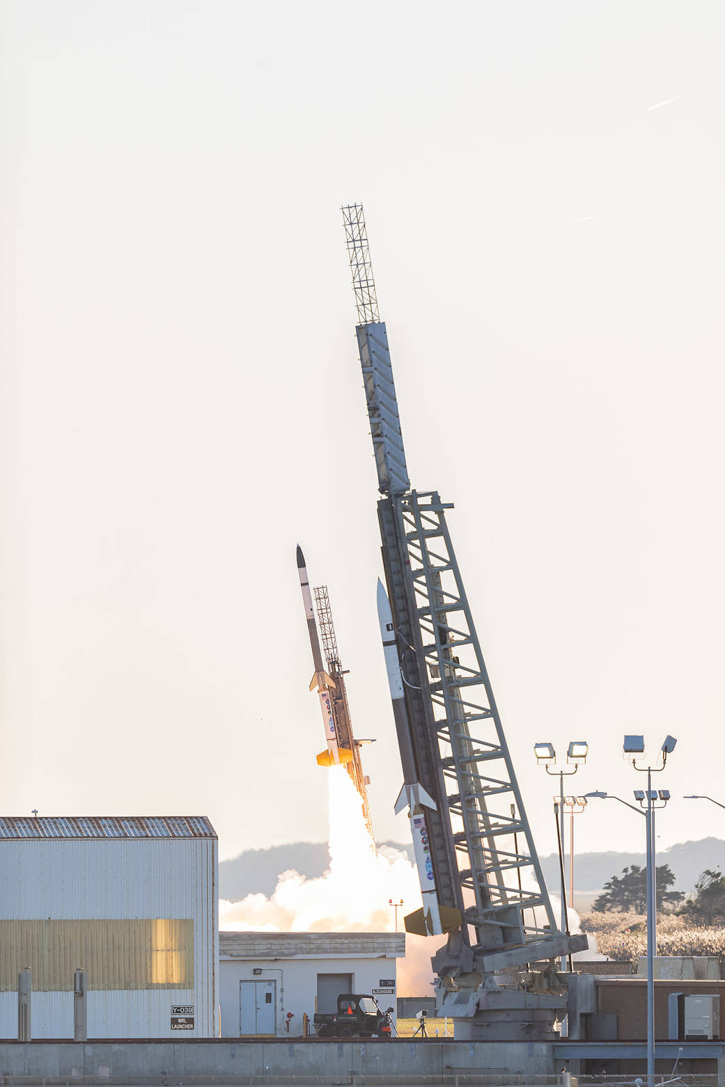 sounding rocket taking off in the background with another sounding rocket on a rocket launcher in the foreground.