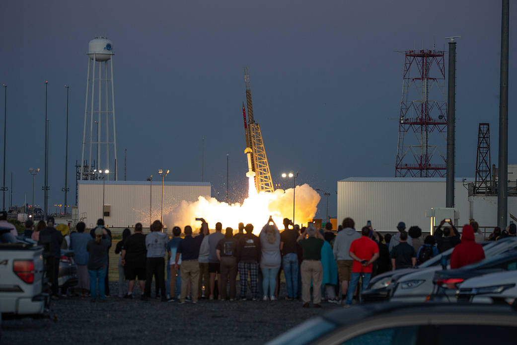 In the foreground, a large group of students watched a sounding rocket take off in the distance.
