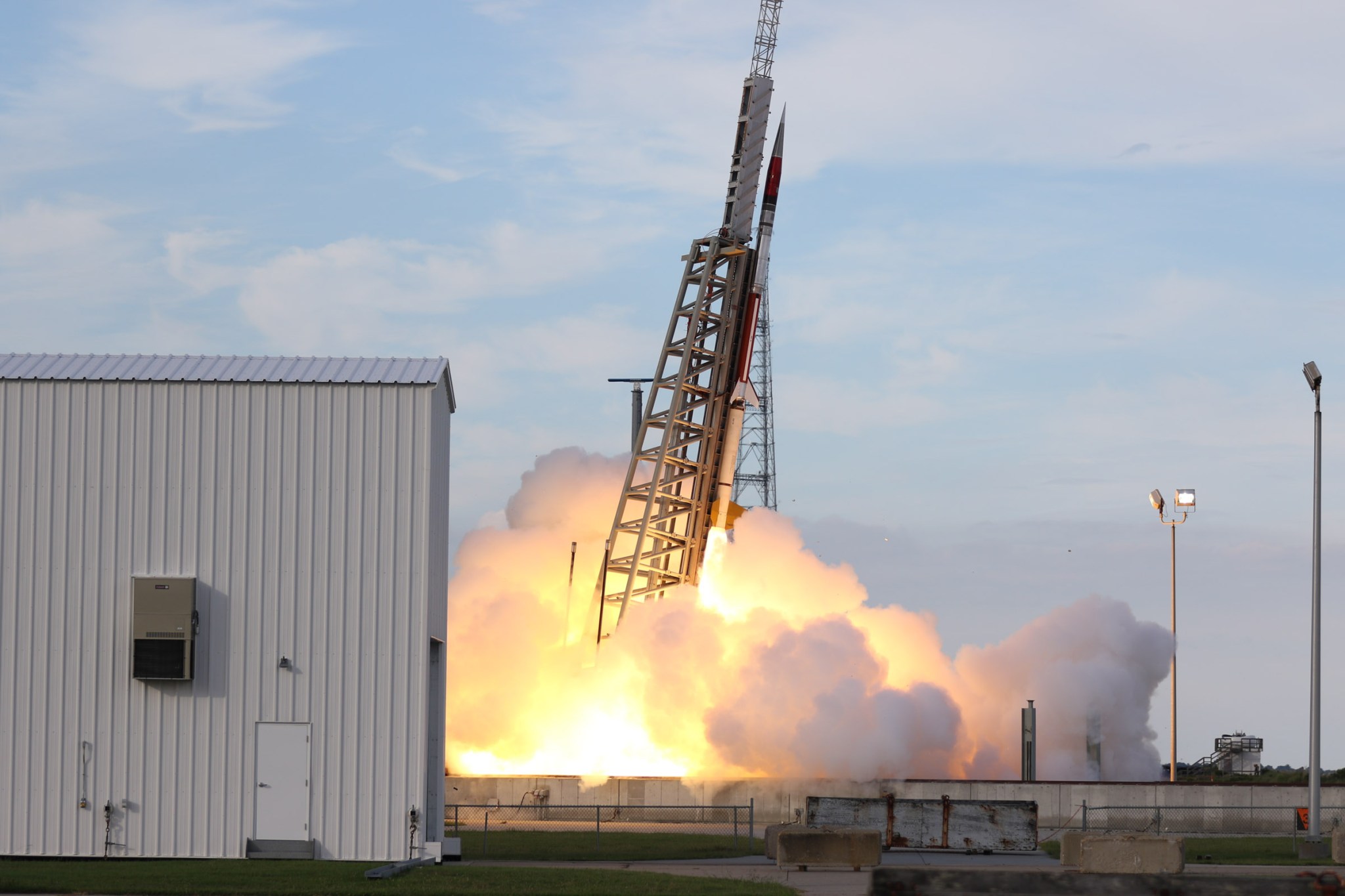 A sounding rocket seconds in mid-launch off the launch pad with a bright white plume underneath. In the background is the Atlantic Ocean with a pale grey sky with no clouds.