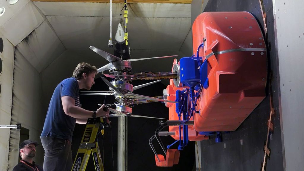 A man in a blue polo shirt working on a full-scale test model of the Dragonfly lander, showing one half of the spacecraft’s structure.