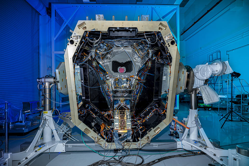 A large metal structure with a thick, silver metal frame stands upright and is open, revealing an interior full of twisted bundles of wires and other metal components. Near the center, a space is open like a smile and a red circle glows from inside it.