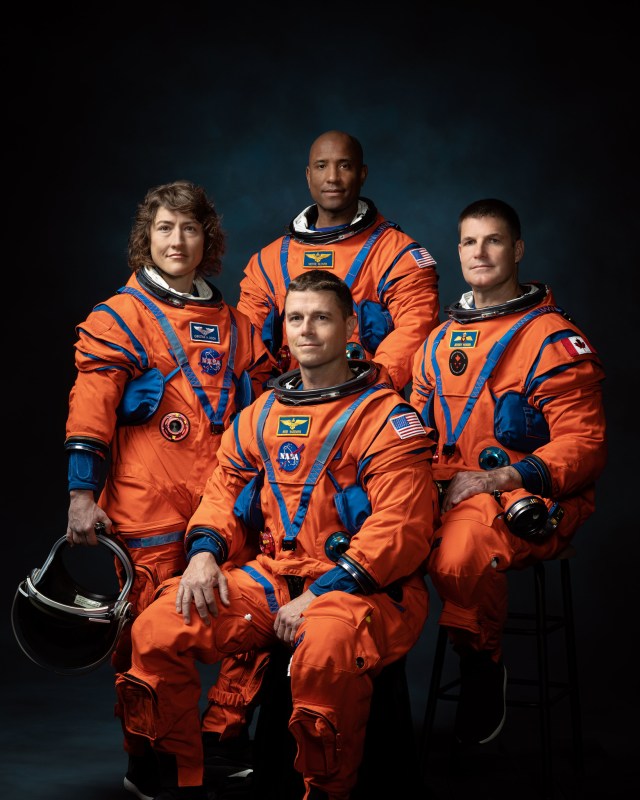 Four astronauts in orange flight suits sit for a portrait