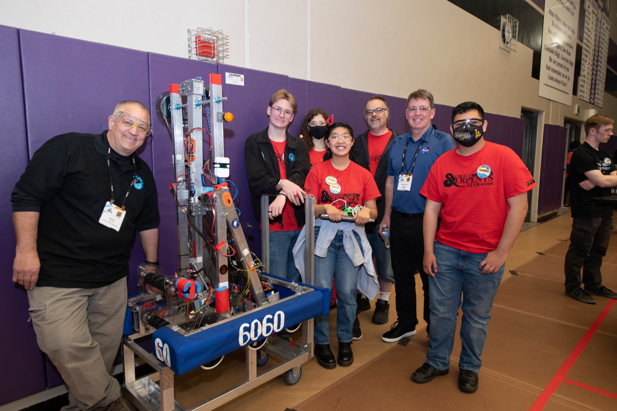 Students and their mentors stand next to a robotics robot.