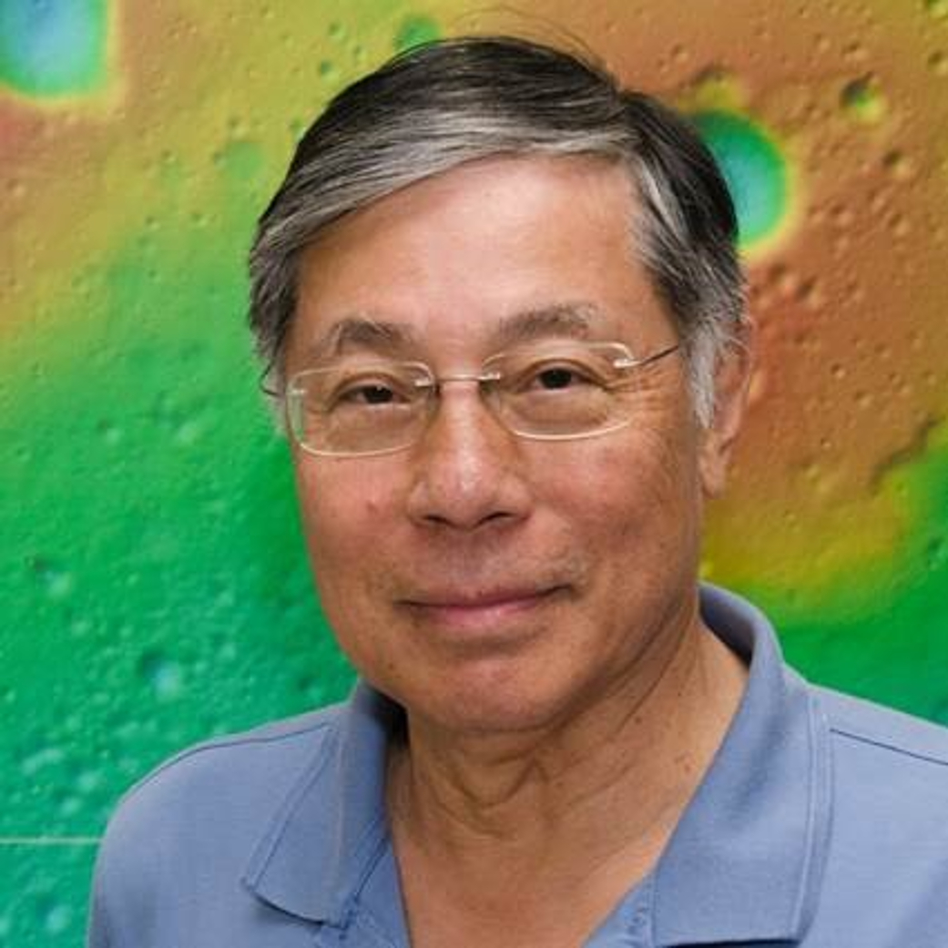 Dr. Gordon Chin, a man with dark hair that fades to silver near his forehead and temples. He wears a light blue shirt and glasses and stands in front of an image of a planet's surface, with surface and craters in shades of orange, yellow, green, and blue.