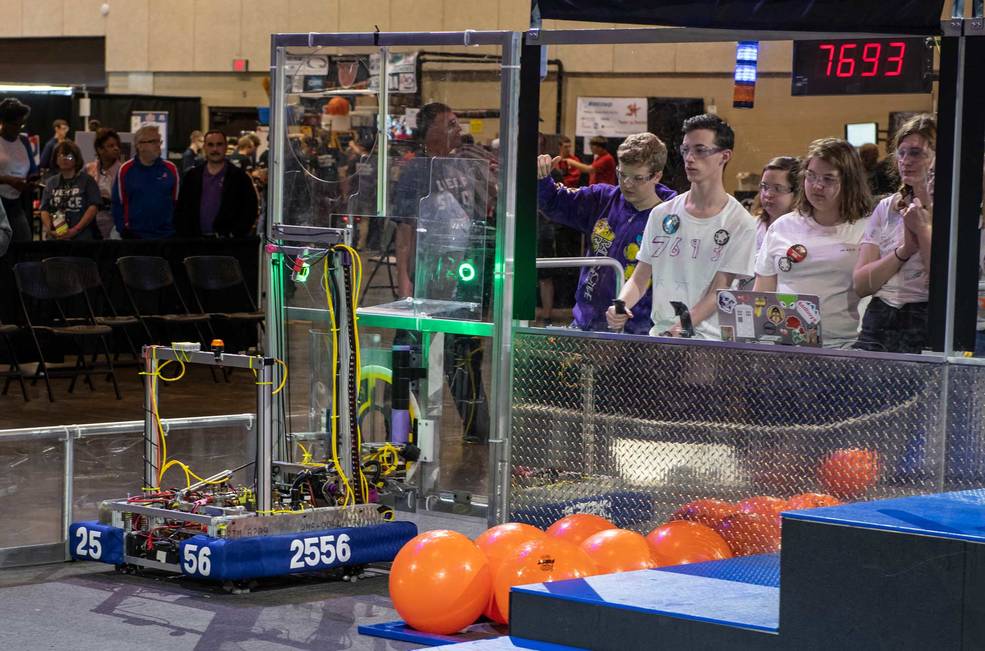 A team looks on as they work with their robot to toss orange balls into the area for the FIRST Robotics competition.