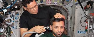 Astronaut Sultan Alneyadi receives a haircut from astronaut Frank Rubio aboard the space station with a hair trimmer containing a suction device collecting loose hair.