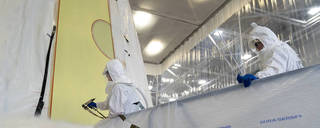 A team member dressed in white apply the first round of spray foam  of NASA’s SLS rocket for Artemis III