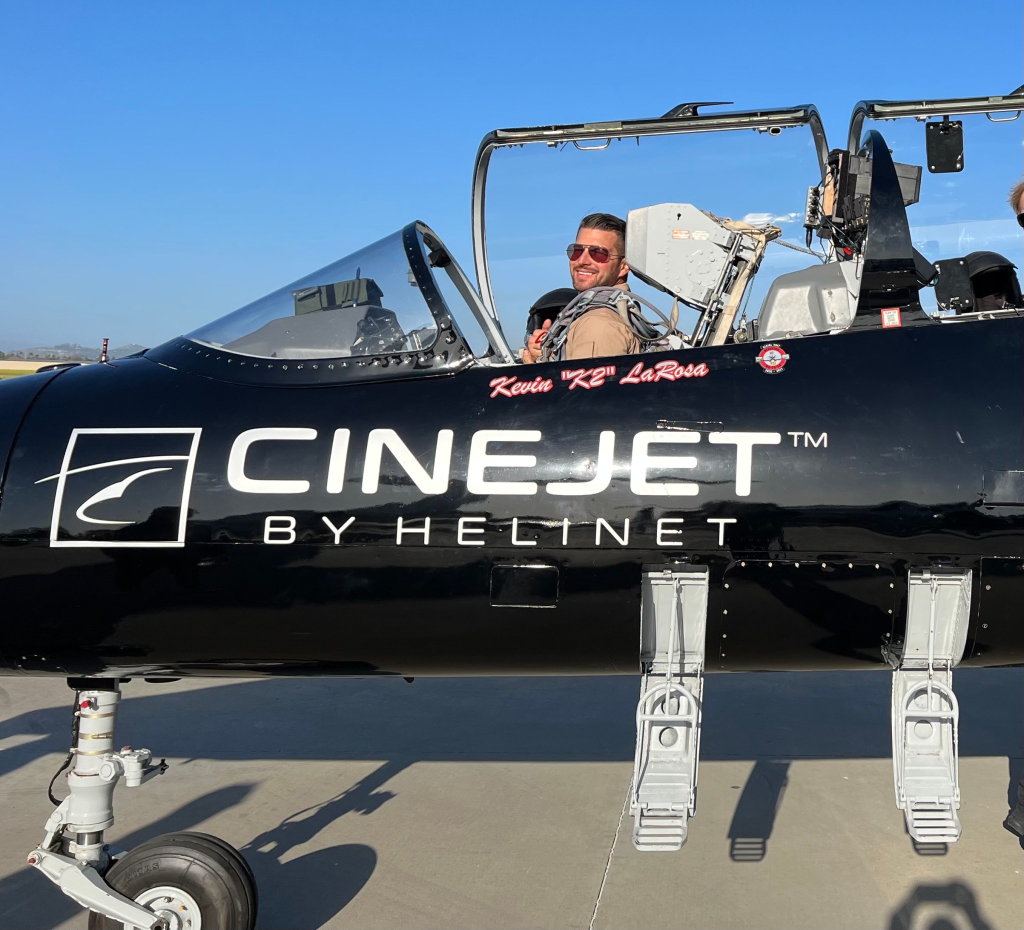 Pilot sits in parked jet with canopy open.