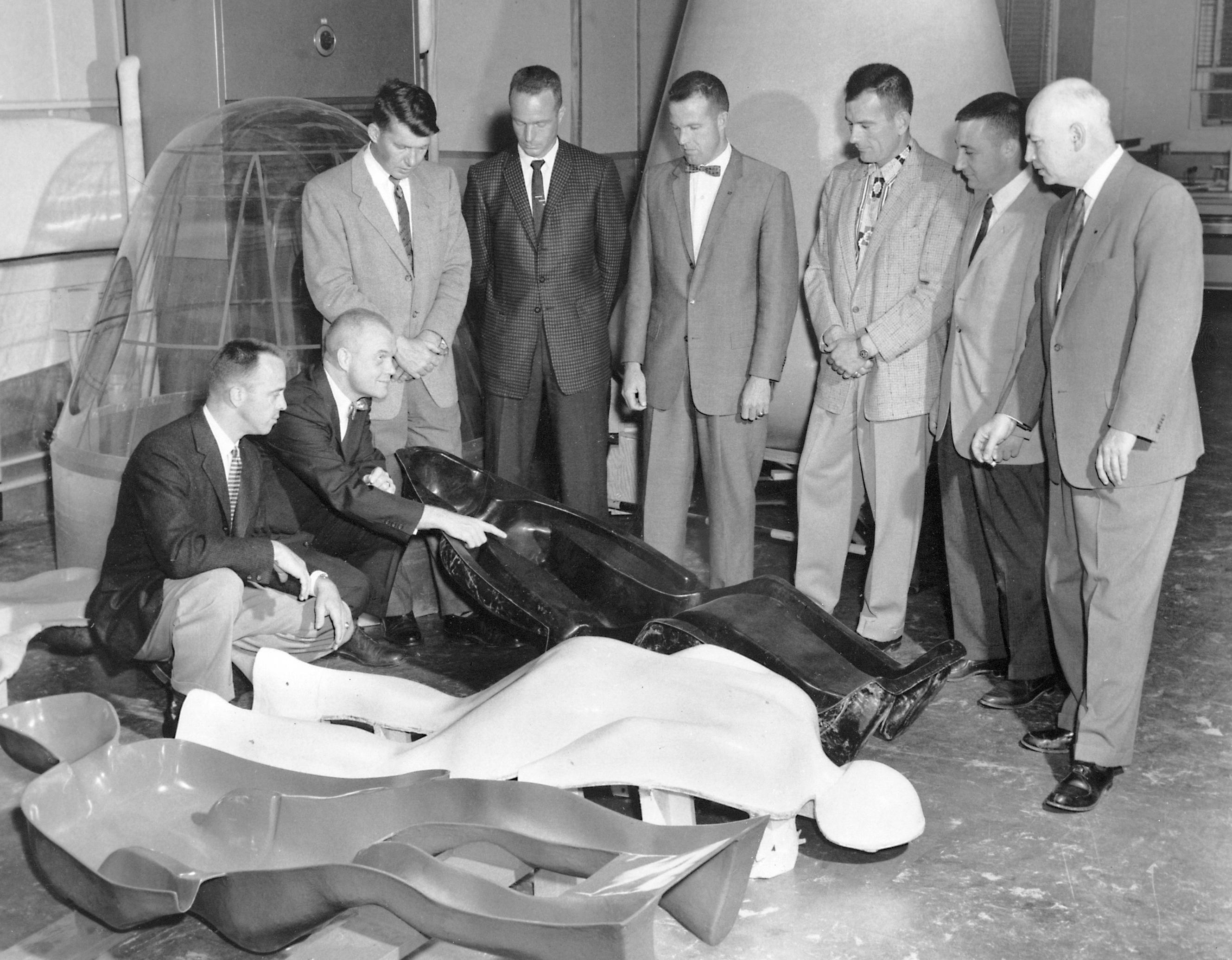 The Mercury 7 astronauts and Bob Gilruth examine an astronaut couch, which was molded to fit each of their bodies to protect them from the G-loads ...