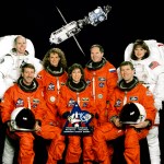 The crew of STS-96 in orange and white space suits pose for portrait
