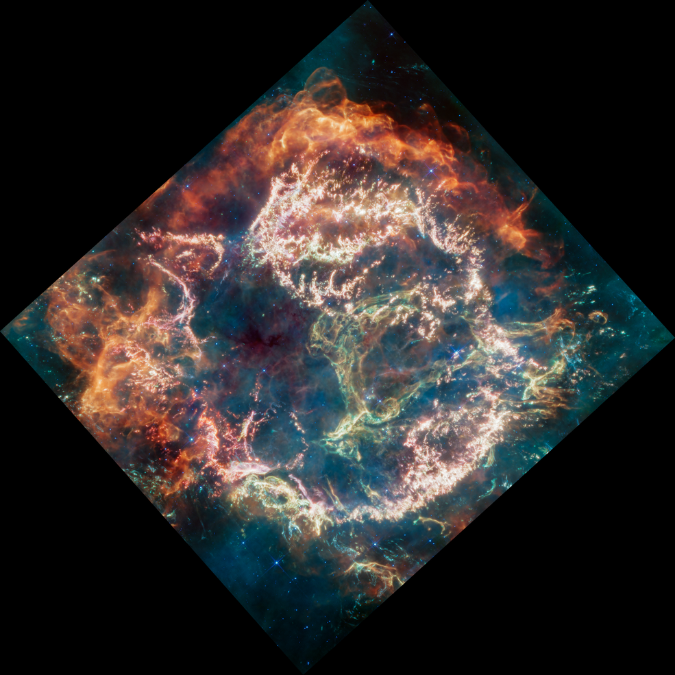 Circular-shaped nebula with complex structure. On its exterior, particularly top and left, are fiery orange curtains of material. Within this is a ring of bright pink filaments. A greenish loop is on right. Blue, green, and red wisps are throughout.