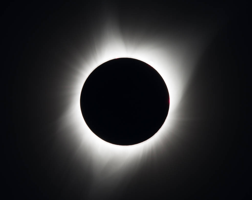 A photo of a total solar eclipse shows the Sun obscured by the Moon, which appears as a black disk, surrounded by the glowing, white corona, all set against a black sky.