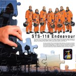 Endeavour STS-118 crew poster showing the crew in orange flight suits, ISS superimposed over a puzzle with a hand putting in another piece