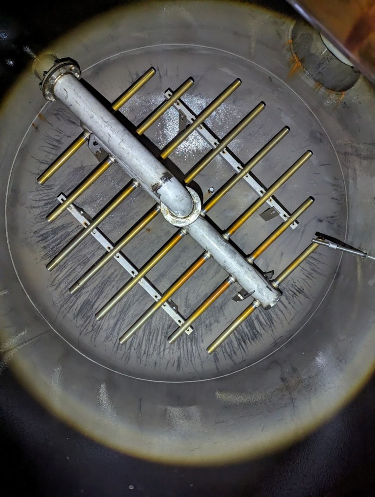 Inside of circular tank are parallel gold tubes with a white pipe running perpendicular.