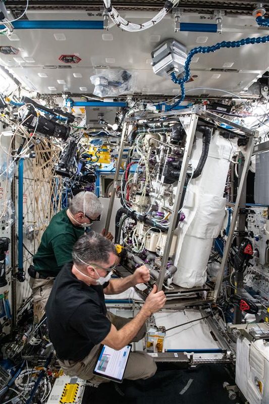Astronauts aboard the ISS in green t-shirts work on the CO2 scrubber