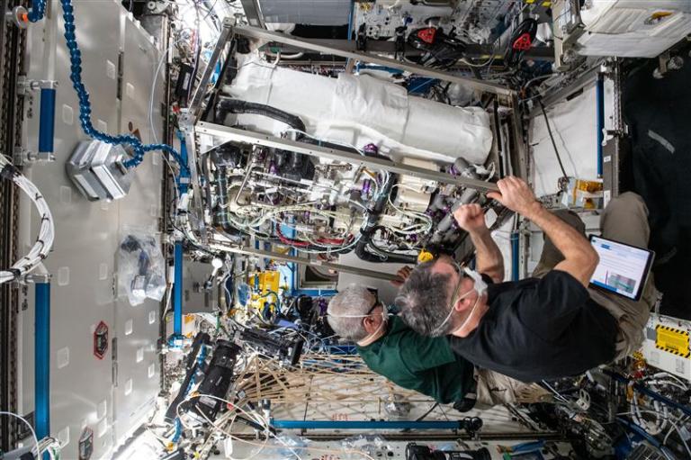 Astronauts aboard the ISS in green t-shirts work on the CO2 scrubber
