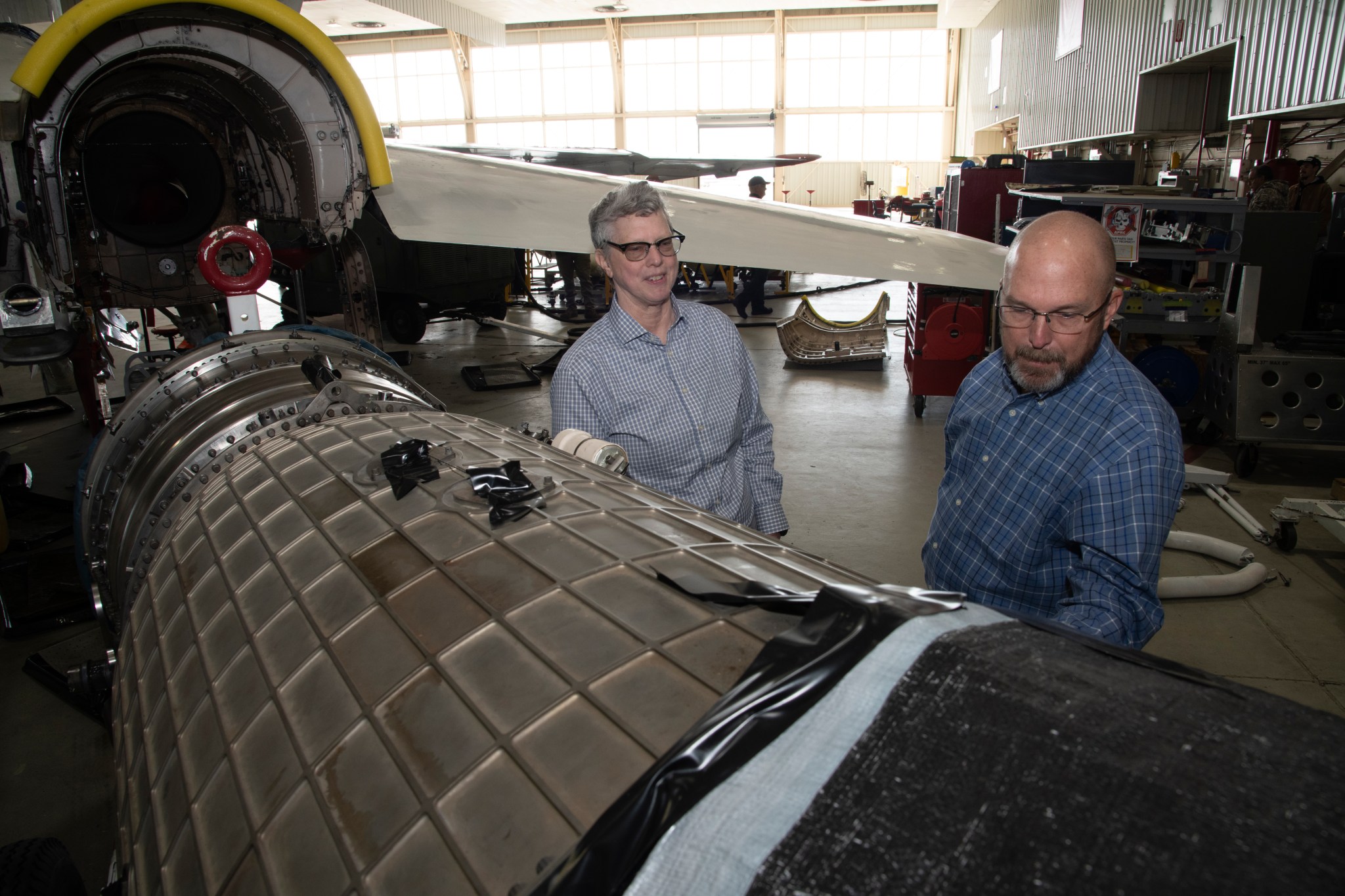 Two people stand next to a huge aircraft engine.