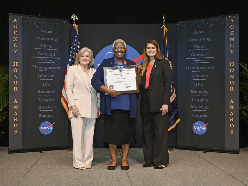 Karen Oliver, center, displays her Distinguished Service Medal and award certificate while standing with Marshall Director Jody Singer, left, and NASA Deputy Associate Administrator Casey Swails. 