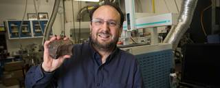A man with glasses holds up a fragment of a meteorite in a lab.